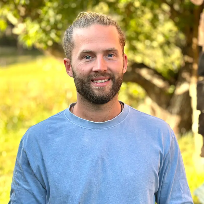 Portrett av Snorre Vikingsen i blå genser, smilende på en solfylt eng.
