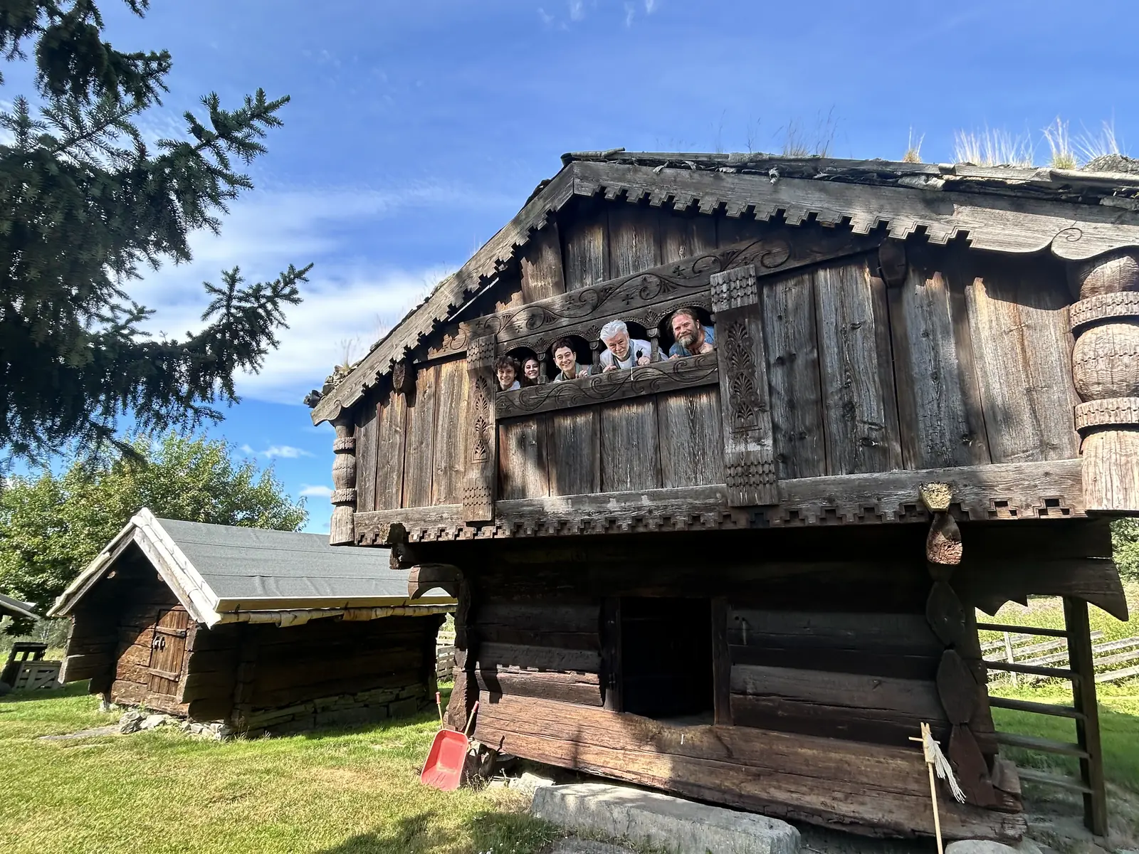Mennesker lener seg ut over den utskårne trebalkongen på et gammelt stabburloft.