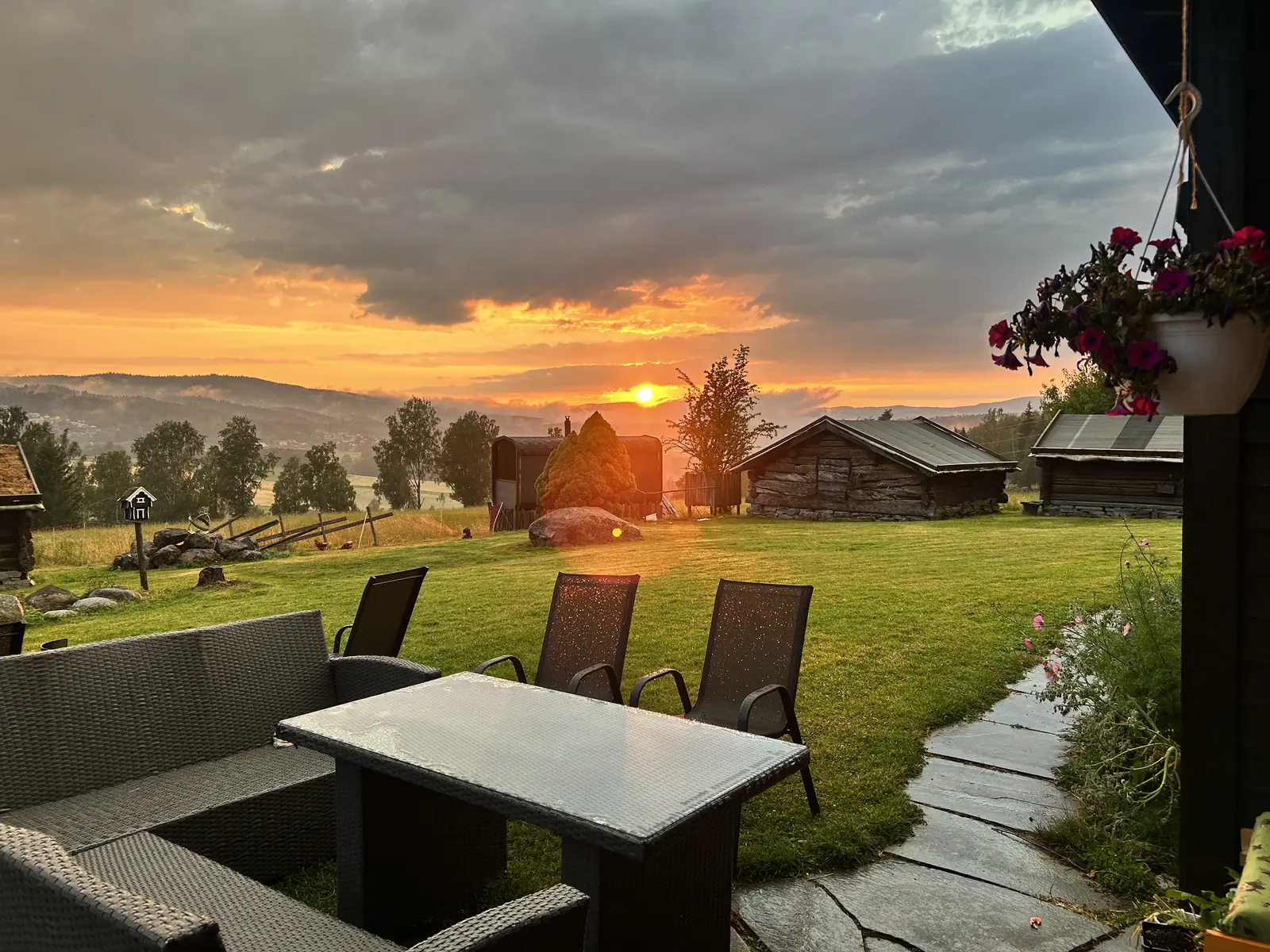 En terrasse med hagemøbler med utsikt over tunet mot en sterk solnedgang.