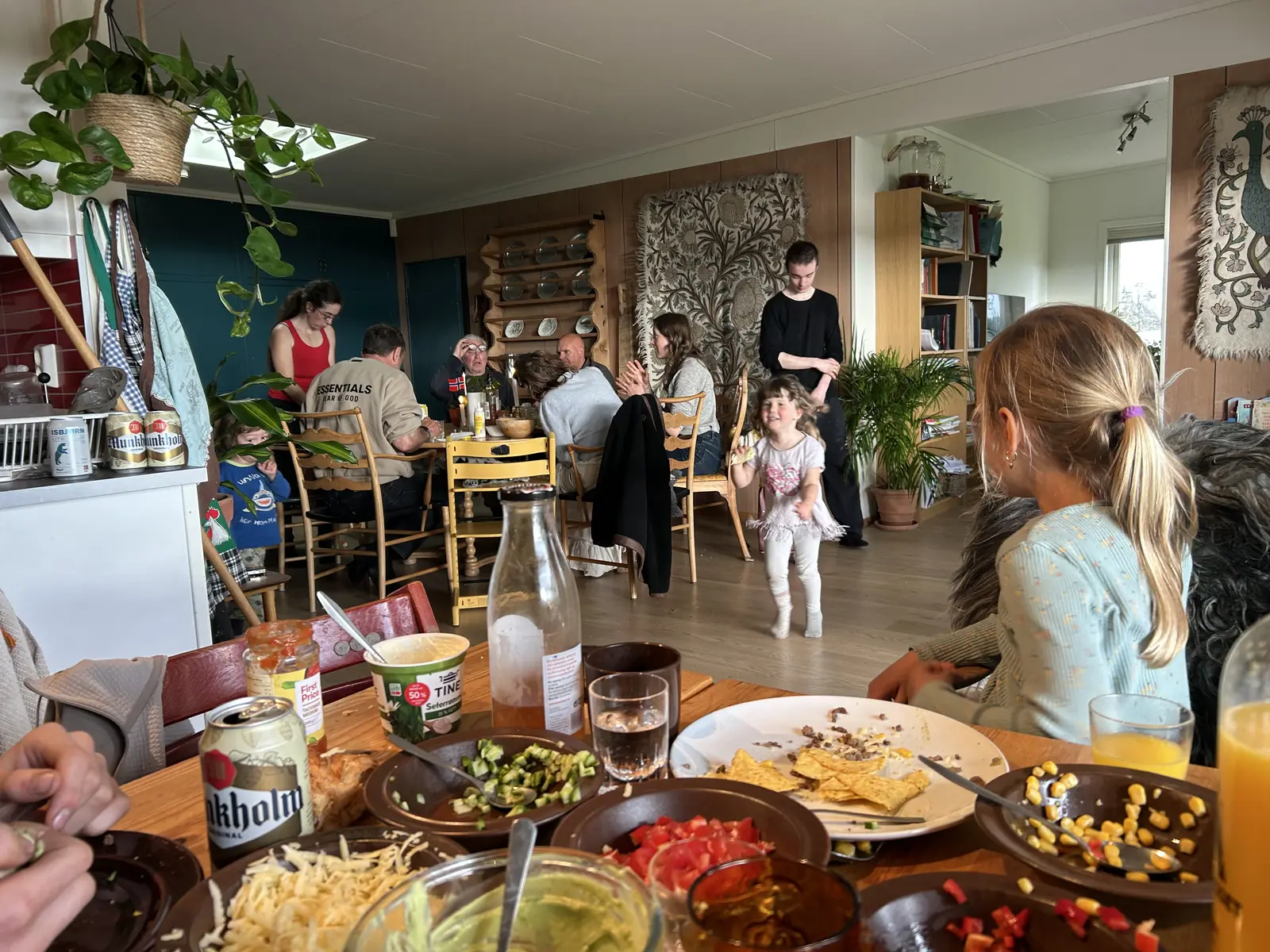 Et måltid rundt et langt trebord i et rustikt kjøkken, med tallerkener og fat delt langs bordet.